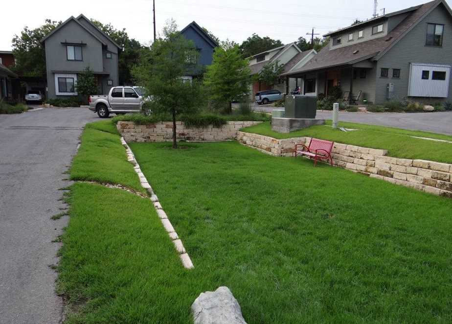 A grassy, three-foot recession with stone walls, a tree and a bench.